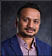 A man wearing a blue jacket and a purple shirt. Description generated by AI